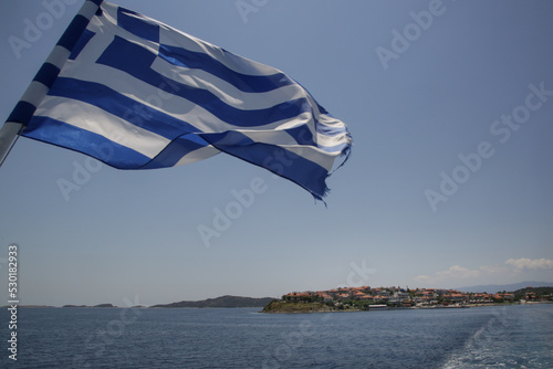 The national flag of Greece waves in the wind at the back of the ferry at sunny day