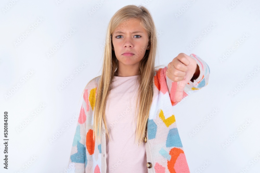 little kid girl wearing colorful yarn jacket over white background looking unhappy and angry showing rejection and negative with thumbs down gesture. Bad expression. little kid girl wearing colorful yarn jacket over white background looking unhappy and angry showing rejection and negative with thumbs down gesture. Bad expression.