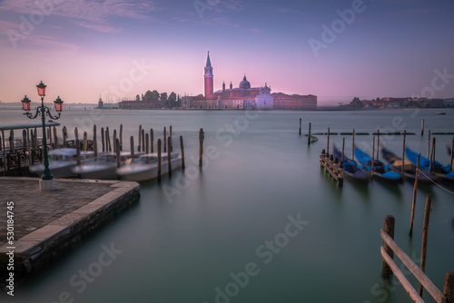 Gondole docked by wooden mooring poles in grand canal, Ethereal Venice, Italy