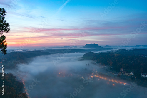 View from viewpoint of Bastei in Saxon Switzerland, to Elbe river and Kurort Rathen at sunrise in the morning fog, National park Saxon Switzerland. Mist over the river Elbe