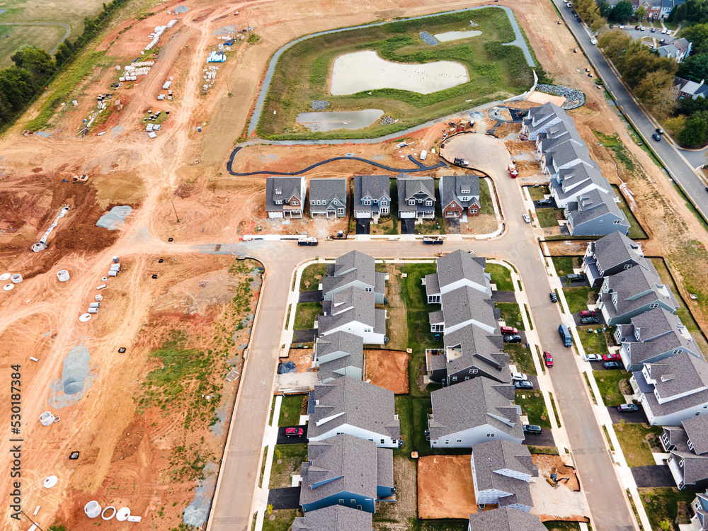 New houses on a construction site and a prepared construction site with stacks of water pipes. Drone view.