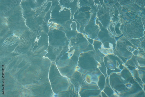 Kleine Wellen in einem mit Wasser gefüllten Pool reflektieren und spiegeln das helle Tageslicht; sie erzeugen irreguläre Muster. Die Wellen werden durch Kinder und den Wind erzeugt. 