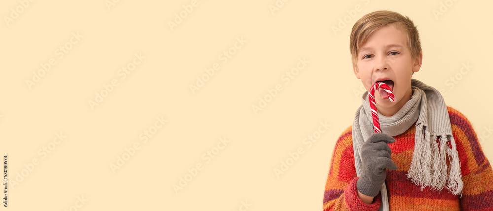 Cute little boy in winter clothes and with candy cane on light beige background with space for text Cute little boy in winter clothes and with candy cane on light beige background with space for text