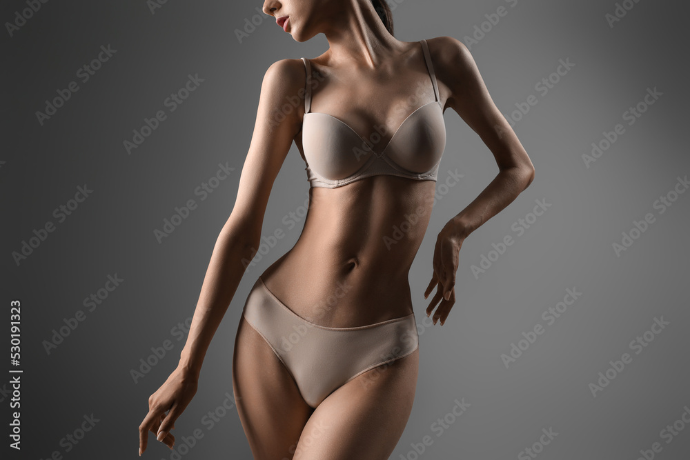 Skinny young woman in underwear on grey background