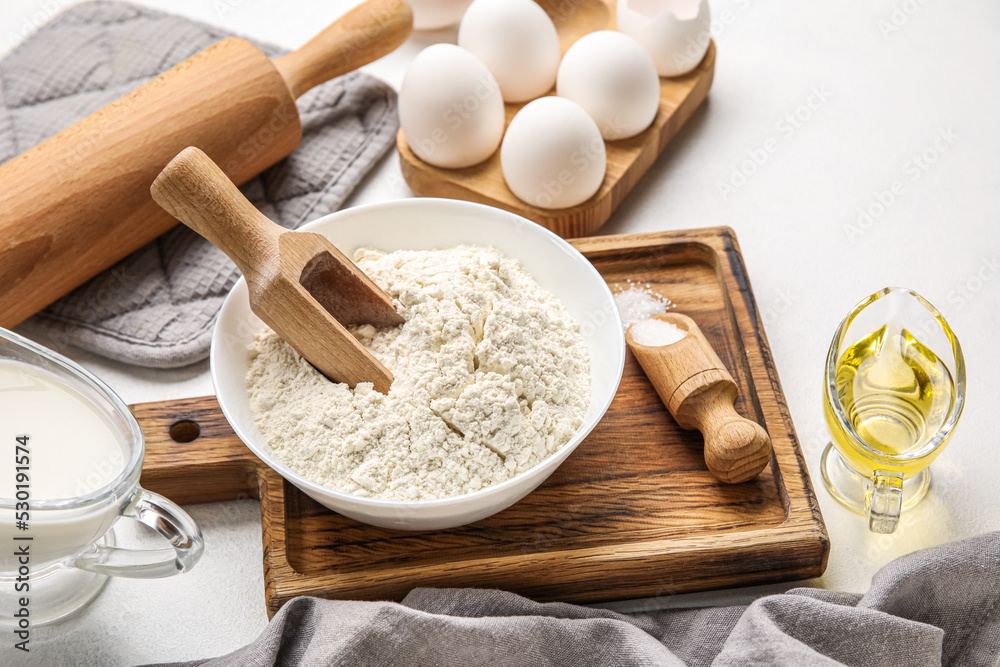 Wooden board with bowl of flour and sugar on table