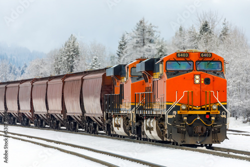 two locomotives pulling a freight train in winter close to Whitefish, Montana with exhaust blurring the trees in the background.