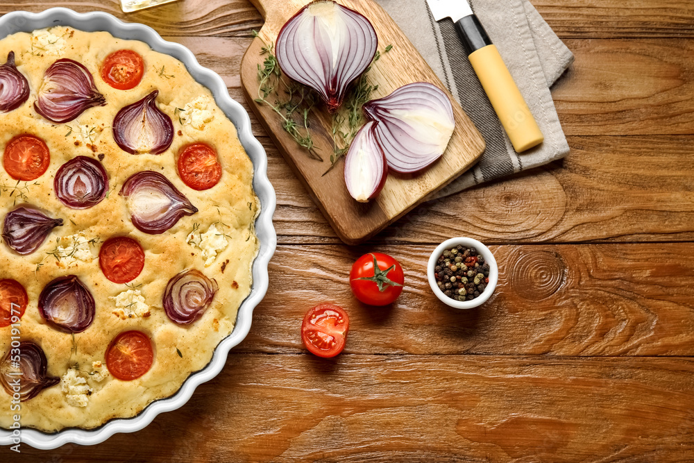 Baking dish with tasty Italian focaccia and ingredients on wooden background Baking dish with tasty Italian focaccia and ingredients on wooden background