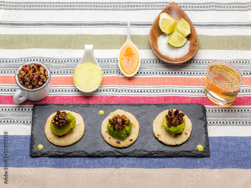 Small avocado sopes with marinated chapulines accompanied by red and green sauce and tequila reposado with lemon slices and salt.