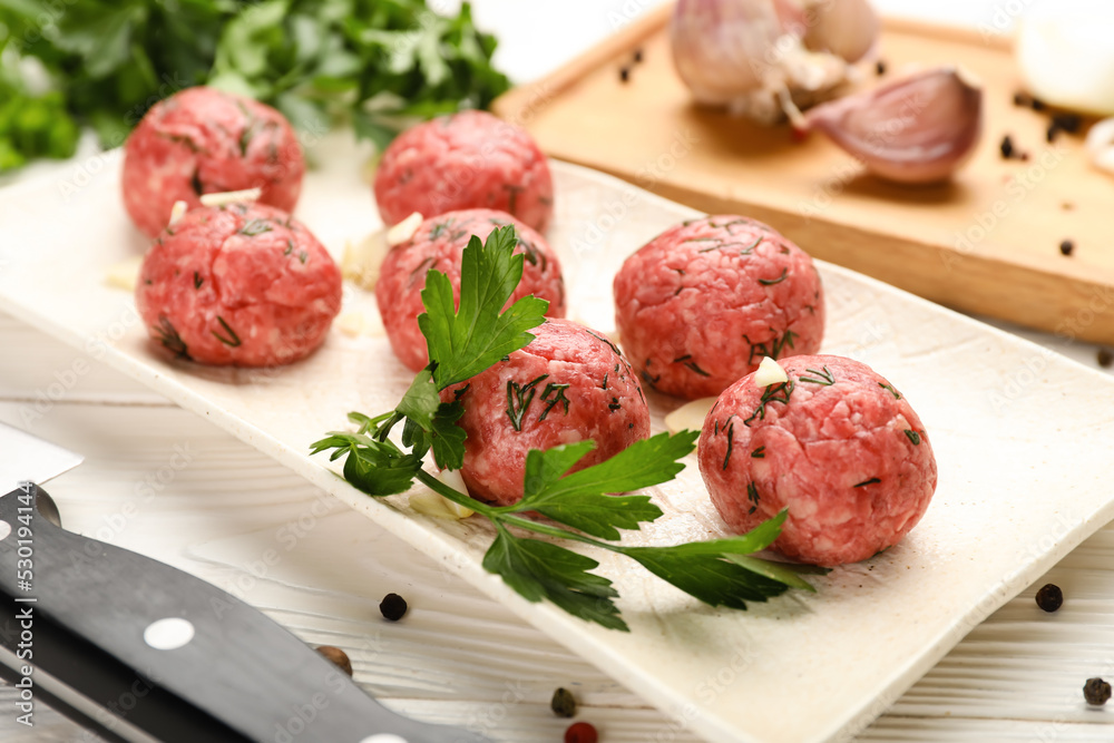 Plate with raw meat balls, parsley, garlic and peppercorns on white wooden background, closeup Plate with raw meat balls, parsley, garlic and peppercorns on white wooden background, closeup