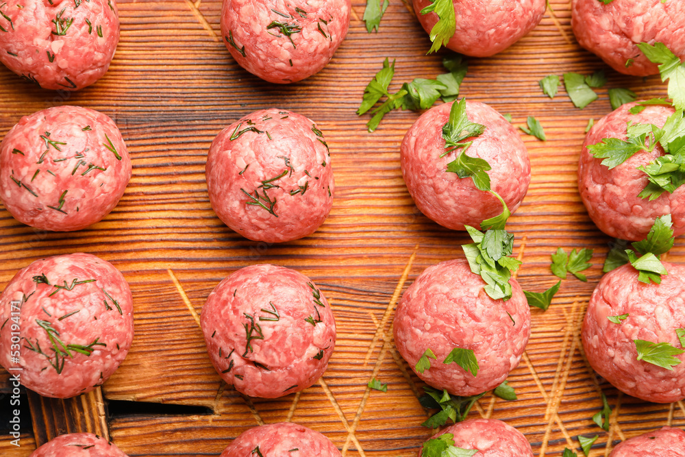 Raw meat balls with cut herbs on wooden board, closeup