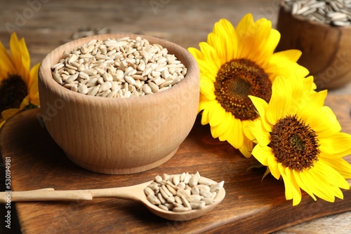 Raw peeled sunflower seeds and flowers on wooden board
