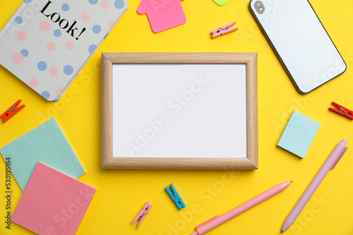 Blank white board with stationery and smartphone on yellow background, flat lay. Space for text