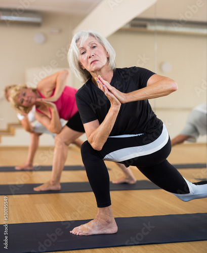 Foto Mature women practicing yoga perform the exercise in the twisted side angle pose