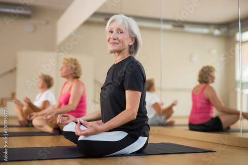 Senior women sitting in lotus pose during their group yoga training.