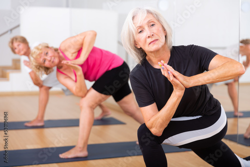 Print op canvas Mature women practicing yoga perform the exercise in the twisted side angle pose
