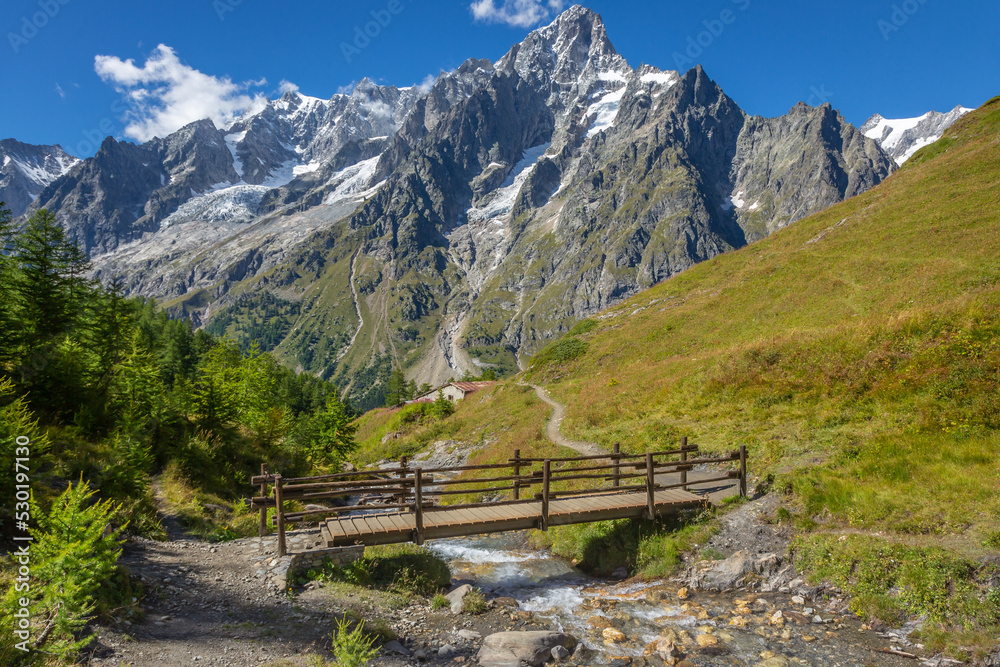 Mont Blanc massif trail into footbridge with river and dramatic landscape, Italy