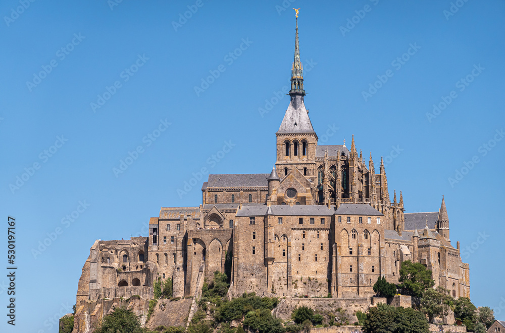 Mont St. Michel, Normandy, France - July 8, 2022: closeup of brown stone religious part, abbay and church on its rock against blue sky.