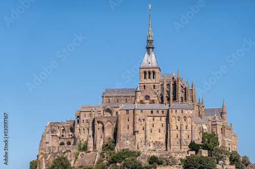 Mont St. Michel, Normandy, France - July 8, 2022: closeup of brown stone religious part, abbay and church on its rock against blue sky. photo