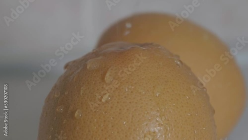 A large grapefruit in the foreground is bathed in water droplets falling in slow motion photo