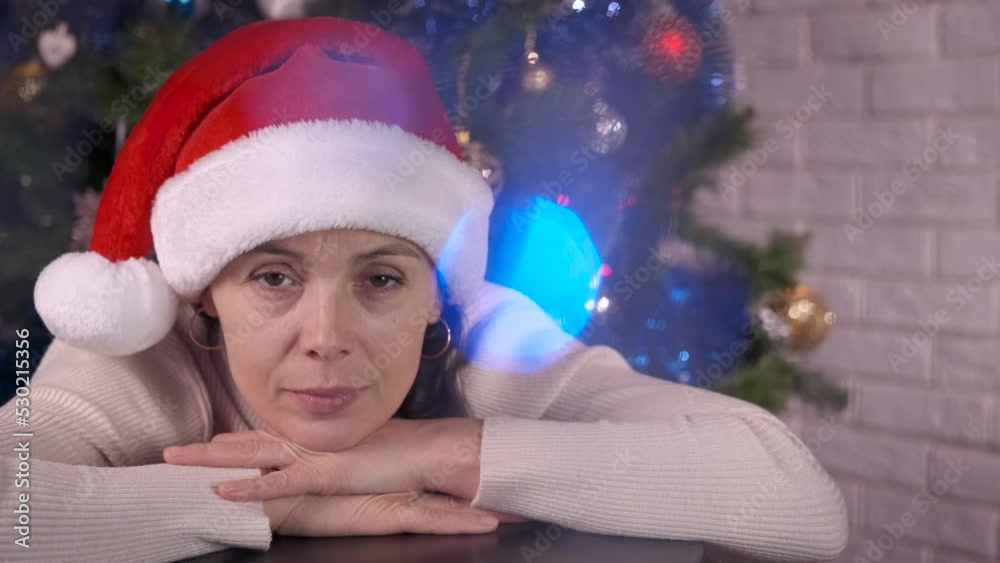 Female alone isolation during Christmas eve. A view of calm woman face in Christmas red hat in the decorated room. Female alone isolation during Christmas eve. A view of calm woman face in Christmas red hat in the decorated room.