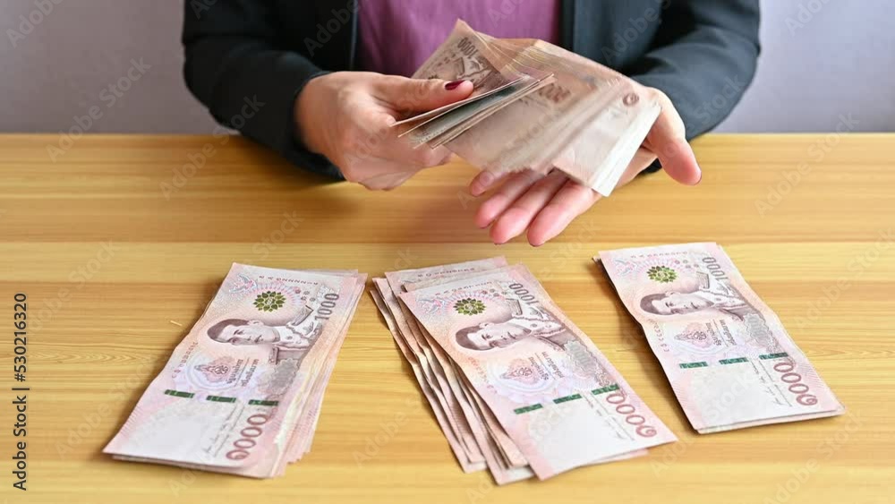 An accountant woman sitting and holding a pile of Thai baht banknotes. The baht is the official currency of Thailand.