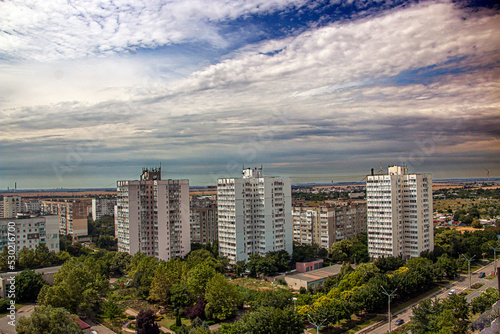 Three sixteen-story houses in the city from a height under a blue sky with clouds among the trees