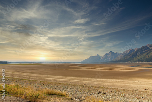 Jackson Lake drought causing receding water and dry lake bed due to global warming at sunrise or sunset in Grand Teton National Park with mountains in background © TS