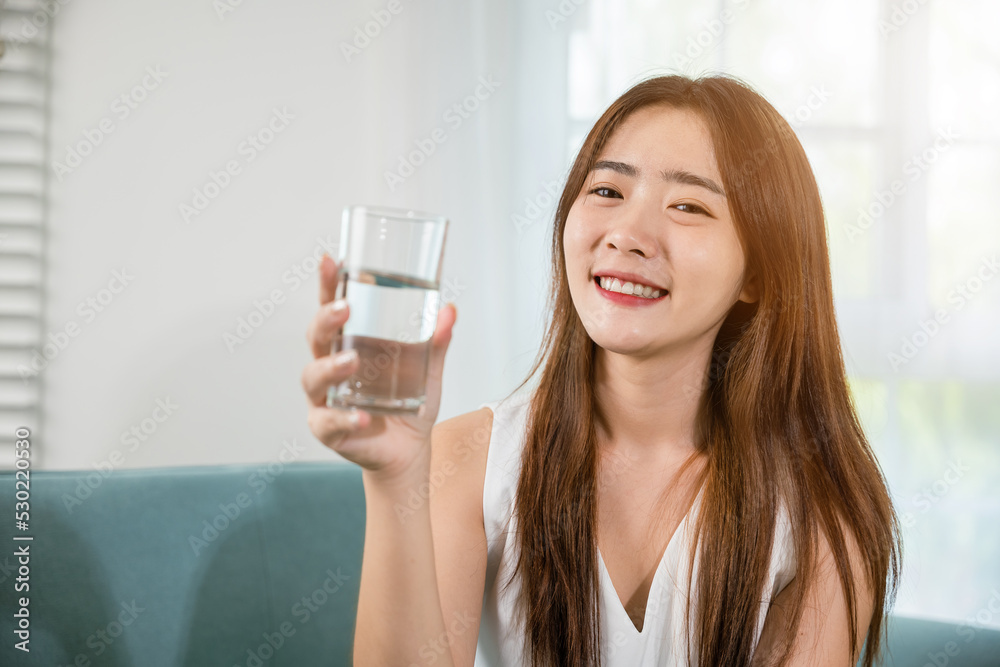 Portrait of Asian young woman holding drinking nature water on hand at home, Happy smiling female beauty with water glass for drink in living room, Healthy lifestyle Portrait of Asian young woman holding drinking nature water on hand at home, Happy smiling female beauty with water glass for drink in living room, Healthy lifestyle