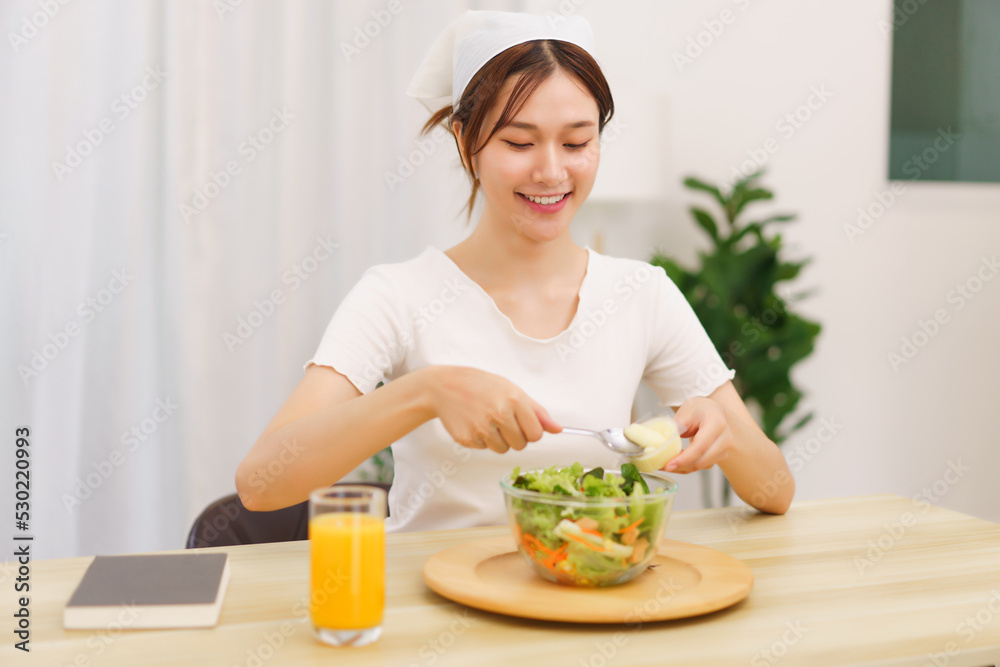Lifestyle in living room concept, Young Asian woman mixing vegetable salad with salad dressing
