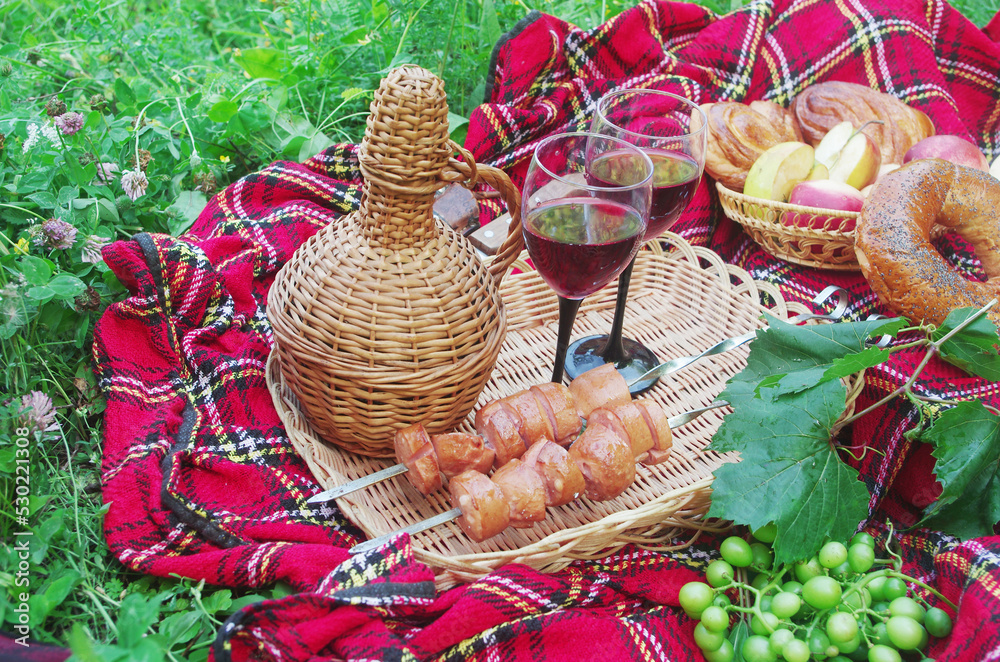 Picnic on the grass. Two glasses of wine, a bottle, fried sausages, fruit, a ukulele, a flute on a spread out blanket.