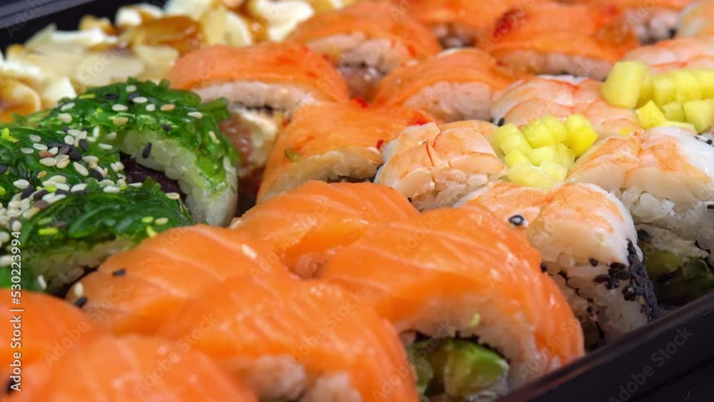 Hand hold chopsticks with sushi roll. Philadelphia roll in sushi set close up. Traditional Japanese food. Japanese kitchen with sea food. Taking one sushi roll from set using sticks for sushi. Hand hold chopsticks with sushi roll. Philadelphia roll in sushi set close up. Traditional Japanese food. Japanese kitchen with sea food. Taking one sushi roll from set using sticks for sushi.