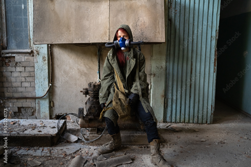 Fototapeta premium Post apocalyptic female survivor in gas mask, destroyed building in the background.
