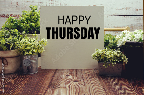 Happy Thursday text message with artificial plant decoration on wooden background