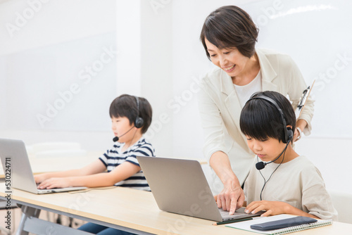 パソコンでプログラミングの授業をする先生と子供（日本人）
