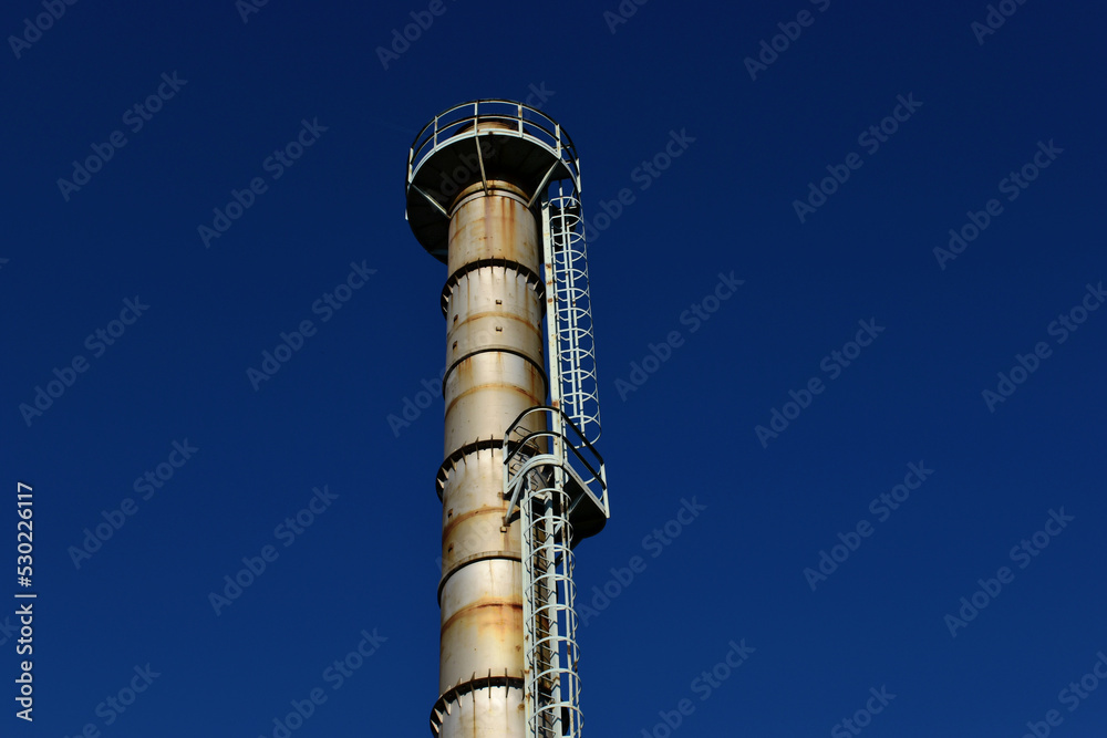 old silver color rusty metal industrial chimney stack. industry and manufacturing concept. grunge detail. exterior access ladder. safety cage. blue sky. Russian gas shortage in Europe concept. old silver color rusty metal industrial chimney stack. industry and manufacturing concept. grunge detail. exterior access ladder. safety cage. blue sky. Russian gas shortage in Europe concept.