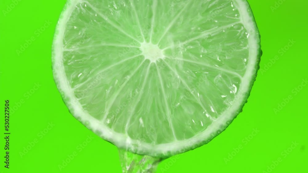 Water drop falling from green hue lime on green background. Lime slice and water splashing, drops of juice falling from juicy fruit. Making cocktail of fruits, drinking cold lemonade. Water drop falling from green hue lime on green background. Lime slice and water splashing, drops of juice falling from juicy fruit. Making cocktail of fruits, drinking cold lemonade.