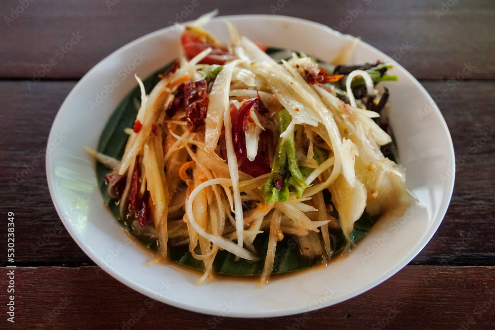 Close-up to papaya salad in a small plate on a wooden table