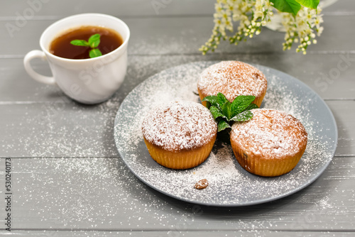 Cupcakes with raisins and a cup of tea, on a background of white flowers.