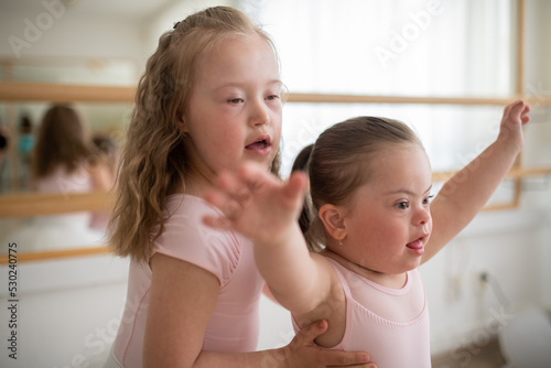 Little sisters with down syndrome dancing ballet in ballet school studio. photo