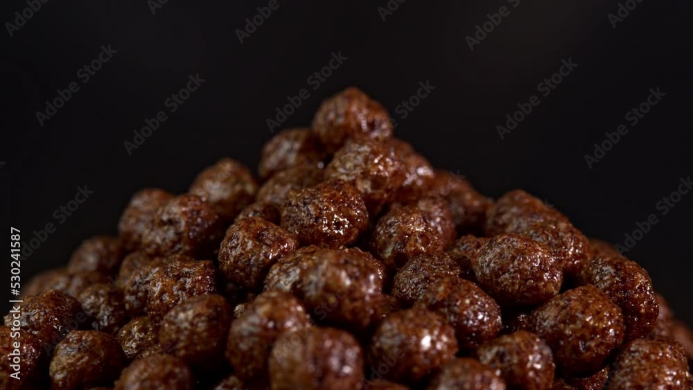 Chocolate cereals rotate on black background. A healthy breakfast spinning in glass. Making cereals chocolate breakfast tasty healthy. Cereals and cereal products flakes pour in a bowl. Chocolate cereals rotate on black background. A healthy breakfast spinning in glass. Making cereals chocolate breakfast tasty healthy. Cereals and cereal products flakes pour in a bowl.