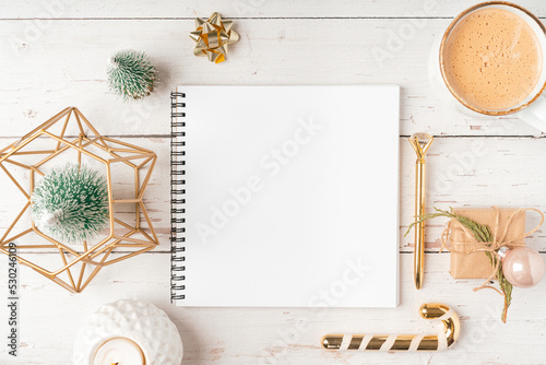Top view Desktop Christmas notepad with mockup blank paper. Flat lay on white wooden table background with planner, coffee cup, tree brunch, Christmas eco nature decoration, notebook and stationery.