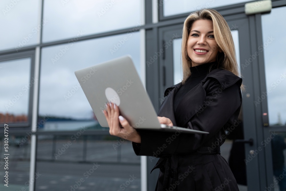 successfully confident businesswoman works online on a laptop against the backdrop of an office building successfully confident businesswoman works online on a laptop against the backdrop of an office building