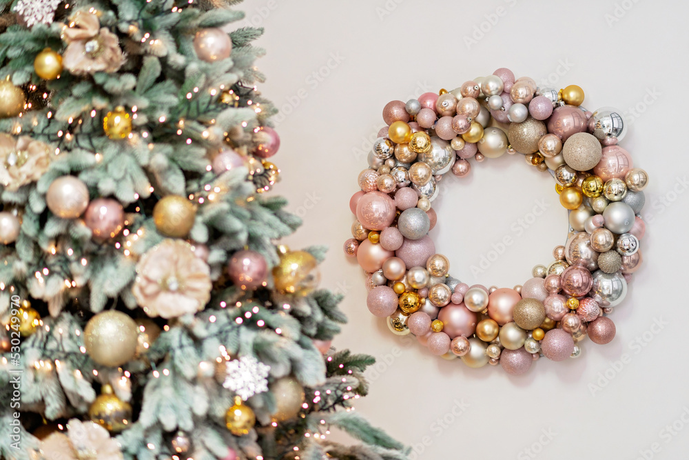 Christmas background, New Year's wreath of sparkling balls in delicate pink colors, and decorated Christmas tree in defocus. Soft selective focus. copy space.