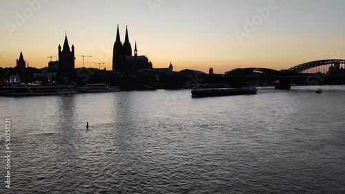 A view of Cologne cathedral as the sun goes down and a barge passes by on the river Rhine