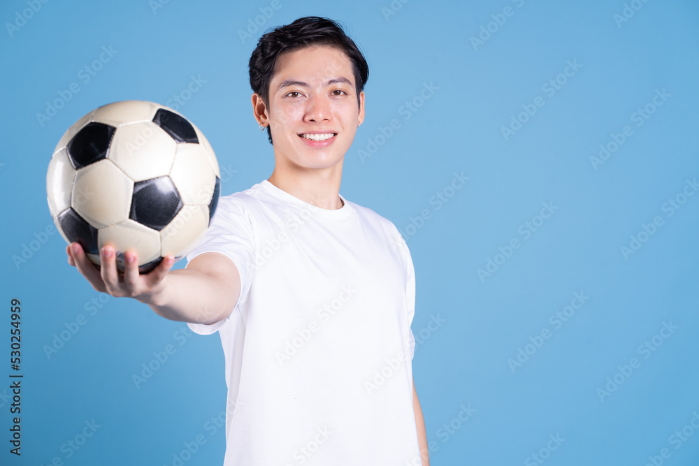 Young Asian man holding ball on background