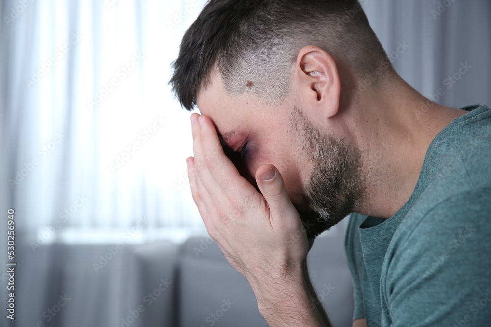 Fototapeta premium Man with bruise on face at home, space for text. Domestic violence victim