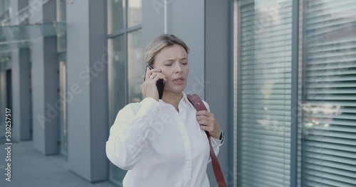 Mature Businesswoman Talking Smartphone Late for Meeting. Confident Lady Looks at Watch Runs to Work Place. Successful Woman in Suit Runs Along Office Building 