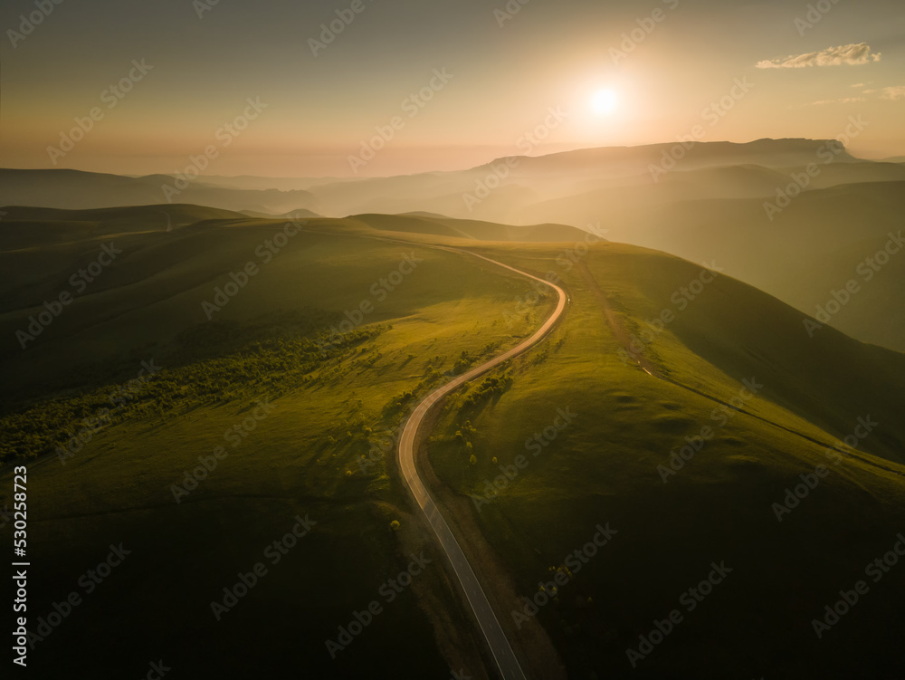 Road in the green hills at foggy sunrise. Gil-Su valley in North Caucasus, Russia.