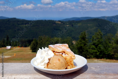 Fototapeta Naklejka Na Ścianę i Meble -  Apple pie with ice cream and whipped cream. Traditional mountain dessert. Szczyrk, Silesian Beskids, Poland. Mountain landscape in the background