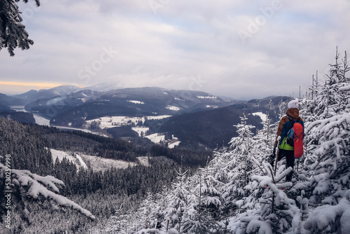 Candid portrait of young smiling man wearing colourful winter hiking jacket, warm-ups and white cap overlooking the snowy area of Stare hamry with the highest point of the Beskydy Mountains Lysa hora photo